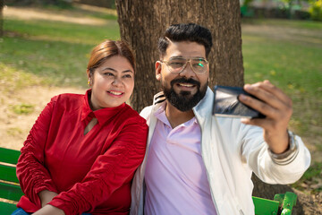 Happy indian couple taking selfie at park.