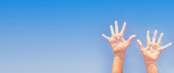 Banner of positive symbol drawing by sunscreen (sun cream, suntan lotion) on two Caucasians open hands on sky background. Concept of protection from sun, skin care, summer vacation. Copy space.