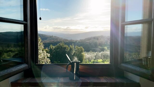 Steaming hot coffee in a espresso maker on a window sill in the morning with a beautiful landscape in the background