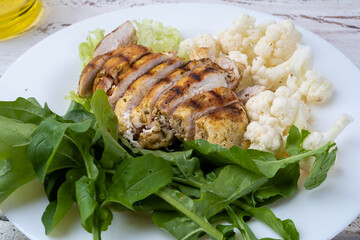 Grilled chicken fillet and sliced served with vegetables and arugula, close-up.