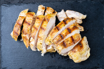 Grilled chicken breast with a beautiful golden crust, barbecue, cut into pieces, top view, dark background, close-up.