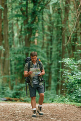 Walking forward with map in hands. Tourist in summer forest. Conception of exploration and leisure
