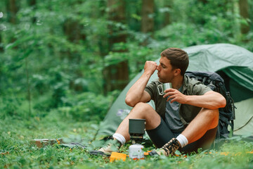 Boiling water, sitting near the tent. Tourist in summer forest. Conception of exploration and leisure