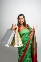 Young Indian woman wearing saree outfit and holding shopping bags on white background.