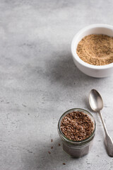 Flax seeds in a glass jar, ceramic a bowl of ground flax for making healthy meals on a gray textured background.