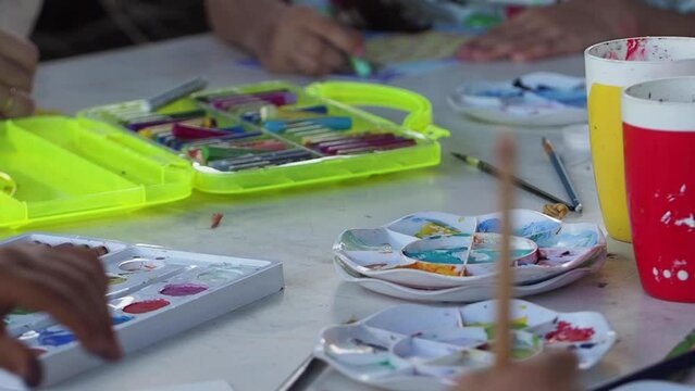 Slow-motion shot of a table with crayons, paints, paintbrushes, and crayons for drawing. Kid's leisure. Art workplace. Education with creativity concept