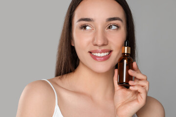 Beautiful young woman with bottle of essential oil on light grey background