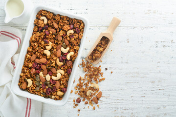 Homemade granola with greek yogurt or milk and cashews, almonds, pumpkin with dried cranberry seeds in old bowl on white rustic wooden table background. Healthy energy breakfast or snack. Top view.