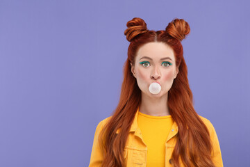 Portrait of beautiful woman with bright makeup blowing bubble gum on violet background. Space for text