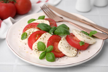 Caprese salad with tomatoes, mozzarella, basil and spices on white table, closeup