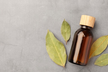 Bottle of bay essential oil and dried leaves on light grey table, flat lay. Space for text