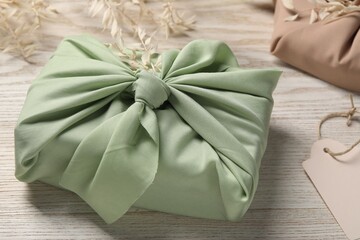 Furoshiki technique. Gift packed in light green fabric and dried branches on white wooden table, closeup