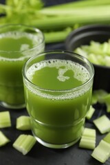 Glasses of delicious celery juice and vegetables on black table, closeup