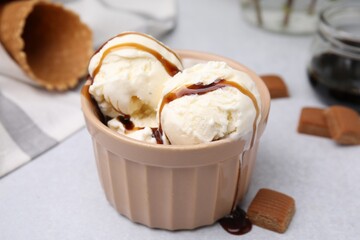 Scoops of ice cream with caramel sauce and candies on light grey table, closeup