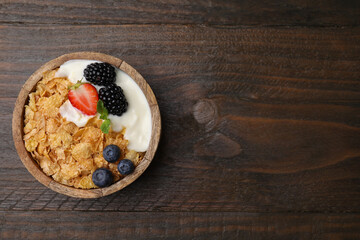 Delicious crispy cornflakes, yogurt and fresh berries in bowl on wooden table, top view with space for text. Healthy breakfast