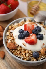 Tasty granola, yogurt and fresh berries in bowl on wooden board, closeup. Healthy breakfast