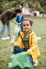 Little cute girl picking up trash plastic bottles in the park. Volunteer concept. Ecology,...