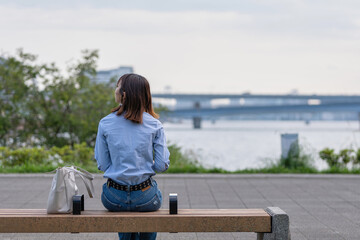 海の近くの公園のベンチに座る女性の後ろ姿 - obrazy, fototapety, plakaty