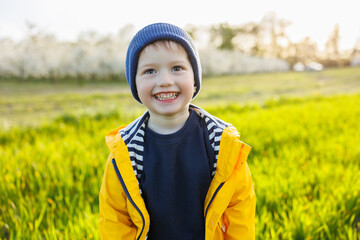 A cute little three-year-old boy in a yellow jacket and cap is running on a green field. A smiling...