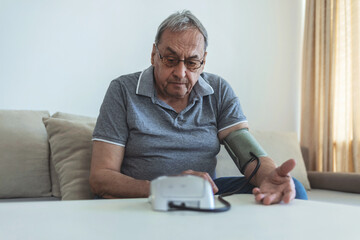 An elderly man measures his blood pressure with a digital meter, he is in the living room and he has a daily routine of checking his heart rate and blood pressure.