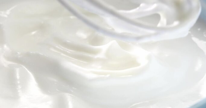 Sour cream is mixed with a whisk in a bowl. Whipping cream. Yogurt texture close up. High angle view. High quality 4k footage.