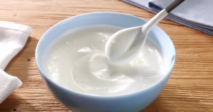 Sour cream is stirred with a spoon in a bowl on a wooden background. Close up. High angle view. High quality 4k footage