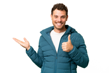 Brazilian man over isolated chroma key background holding copyspace imaginary on the palm to insert an ad and with thumbs up