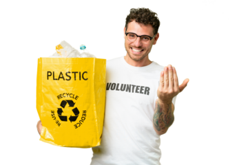 Brazilian man holding a bag full of plastic bottles to recycle over isolated chroma key background inviting to come with hand. Happy that you came