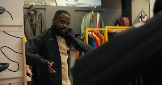 Exploring Style: African American Guy Trying on a Black Windbreaker in Outdoor Gear Store