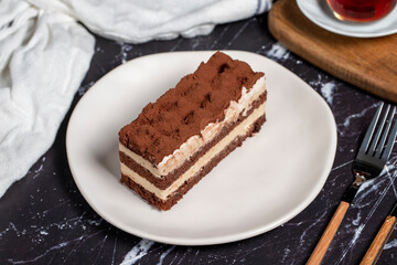 Traditional italian dessert tiramisu cake. Slice of chocolate cake with tiramisu cream and cocoa powder on dark table.