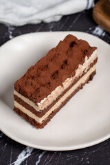 Traditional italian dessert tiramisu cake. Slice of chocolate cake with tiramisu cream and cocoa powder on dark table.