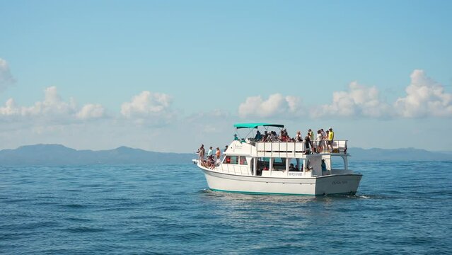 Large motor boat with tourists on board on whale watching excursion. Calm blue surface of water and mountains in the background