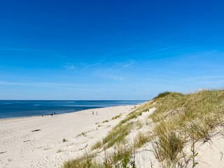 white sea dunes with some dry grass, clear blue sea