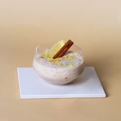 Creamy rice pudding with cinnamon and lemon on white podium at beige background; dessert made from rice, milk, eggs for modern restaurant menu