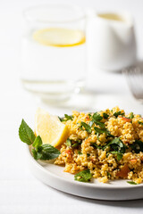 Salad made with bulgur, chopped parsley, tomatoes, mint, onion and seasoned with olive oil and lemon juice on the restaurant table with glass of water