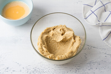 A glass bowl with dough and a bowl of eggs on a light blue background. The stage of making homemade choux dough