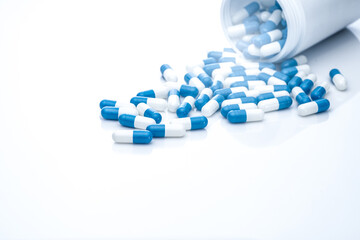 Blue-white antibiotic capsule pills spread out of plastic drug bottles. Antibiotic drug resistance. Prescription drugs. Healthcare and medicine. Pharmaceutical industry. Pharmacy product. Medication.