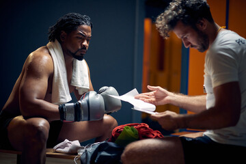 Determined boxing player with serious face in sweats after workout resting with his coach, getting...
