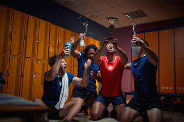 Football team players celebrating success in the dressing room, holding gold medal, shouting and splashing water.