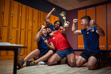 Fototapeta na wymiar Young football players celebrating success together, hugging and cheering, holding golden trophy, feeling victorious in the dressing room.