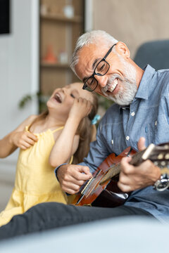 Grandfather laughing as his granddaughter pretends to play guitar with him