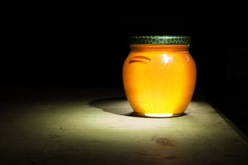 a jar of honey illuminated by light with a black background