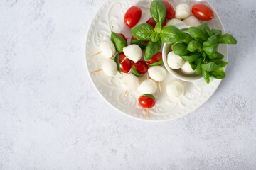 Mozzarella cheese balls, tomatoes, basil leaves and peppercorns for caprese salad flying on white background.