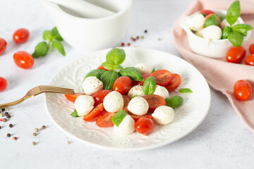 Italian caprese salad with sliced tomatoes, mozzarella, basil, olive oil on a light background.