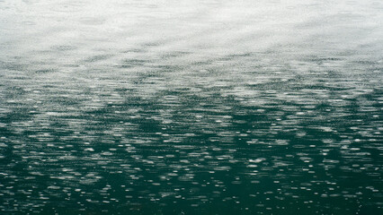 Fototapeta premium Raindrops on water surface. Raindrops falling on teal colored water. Minimal background.