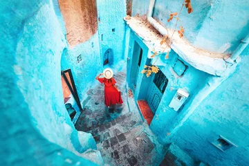 Stoff pro Meter Young woman with red dress visiting the blue city Chefchaouen, Marocco - Happy tourist walking in Moroccan city street - Travel and vacation lifestyle concept © Davide Angelini