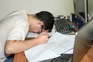 Fototapeta na wymiar Young man with glasses with his head on desk on top of papers stressed by his studies