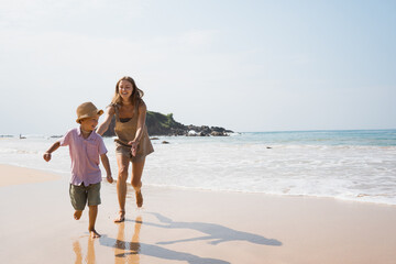 beautiful mother playing and having fun with son on sea cost in summer vacation