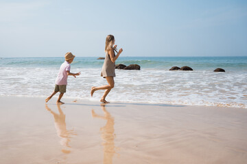 Fototapeta na wymiar Beautiful young mother and son runing outside. beach vibes in sunny day