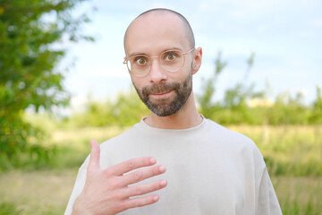 young positive charismatic man in beautiful gold-rimmed glasses, beige t-shirt looking at camera,...